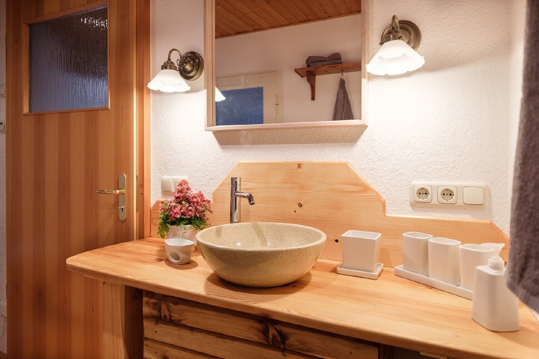A wooden bathroom vanity with a bowl sink, a mirror, and two wall-mounted light fixtures.