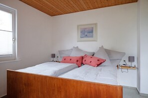 Un dormitorio con estructura de cama de madera, ropa de cama blanca y un cuadro en la pared.