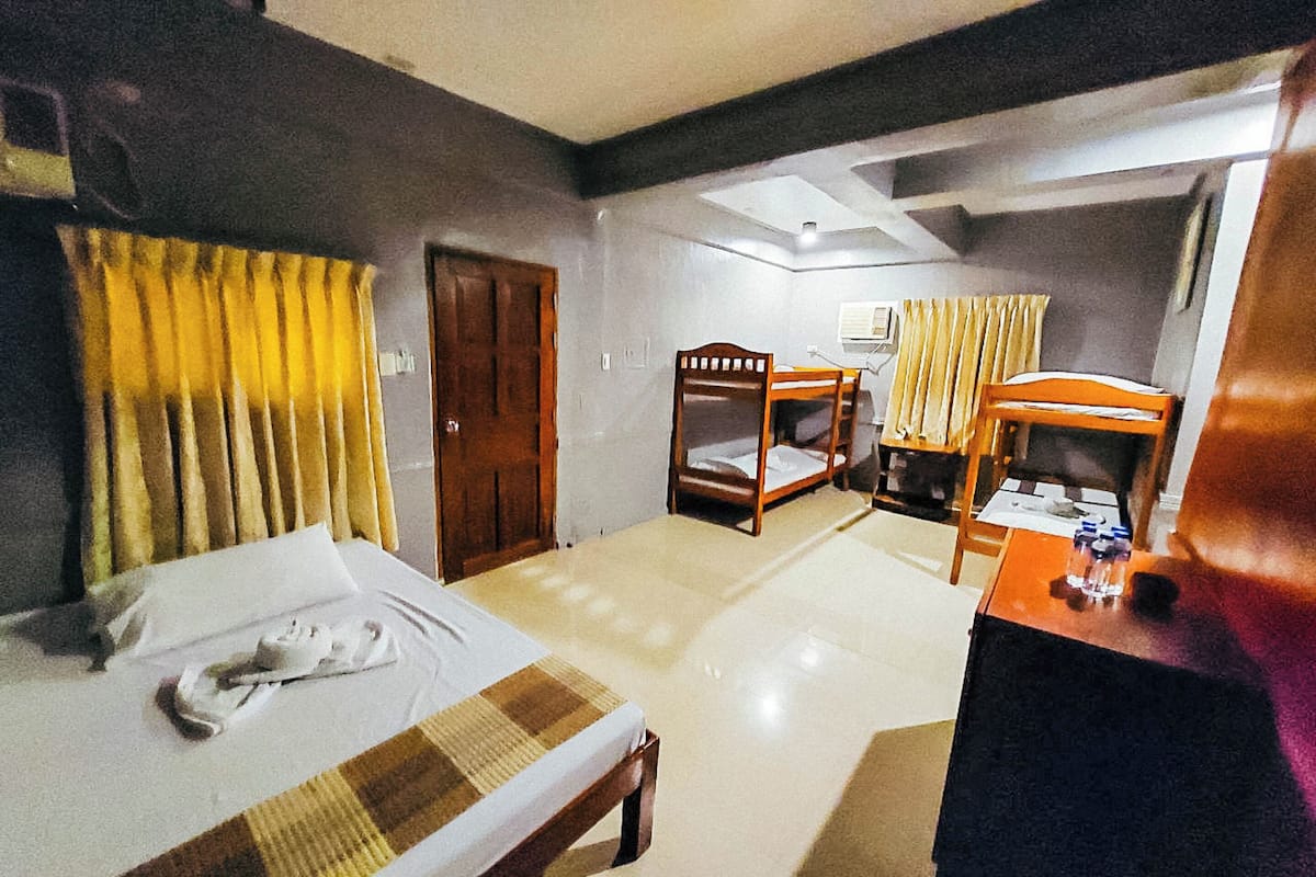 Ein Hotelzimmer mit einem Bett, einem Holzstuhl, einem Schreibtisch mit Stuhl und einem Fenster mit Vorhängen.