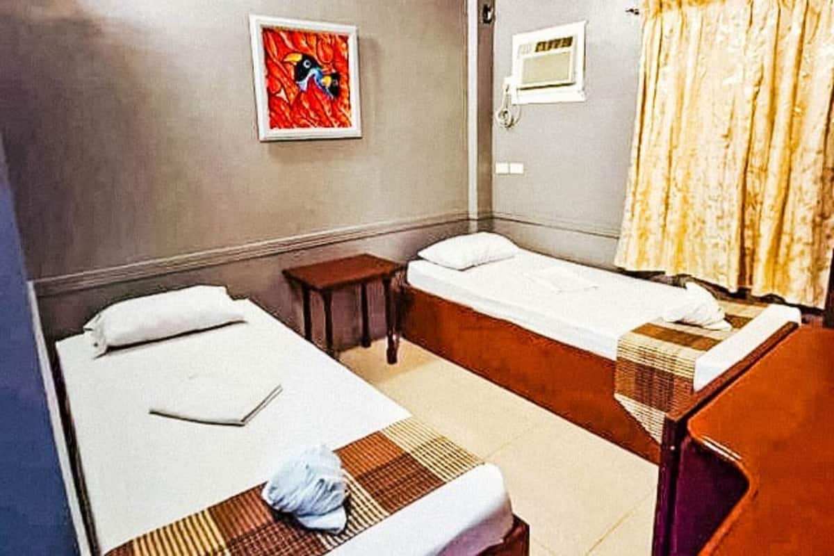 Ein Hotelzimmer mit zwei Einzelbetten, einem kleinen Tisch, einem Stuhl, einem Bild an der Wand und einem Fenster mit Vorhängen.