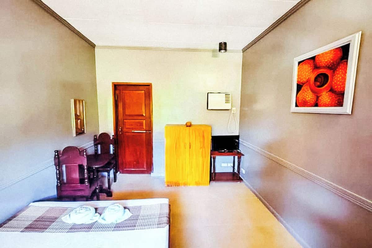Ein Hotelzimmer mit einem Bett, einer Holztür, einem gelben Vorhang, einem kleinen Tisch und einem gerahmten Bild an der Wand.