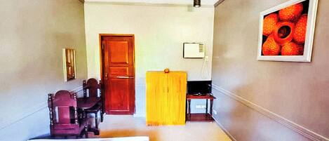 A hotel room with a bed, a wooden door, a yellow curtain, a small table, and a framed picture on the wall.