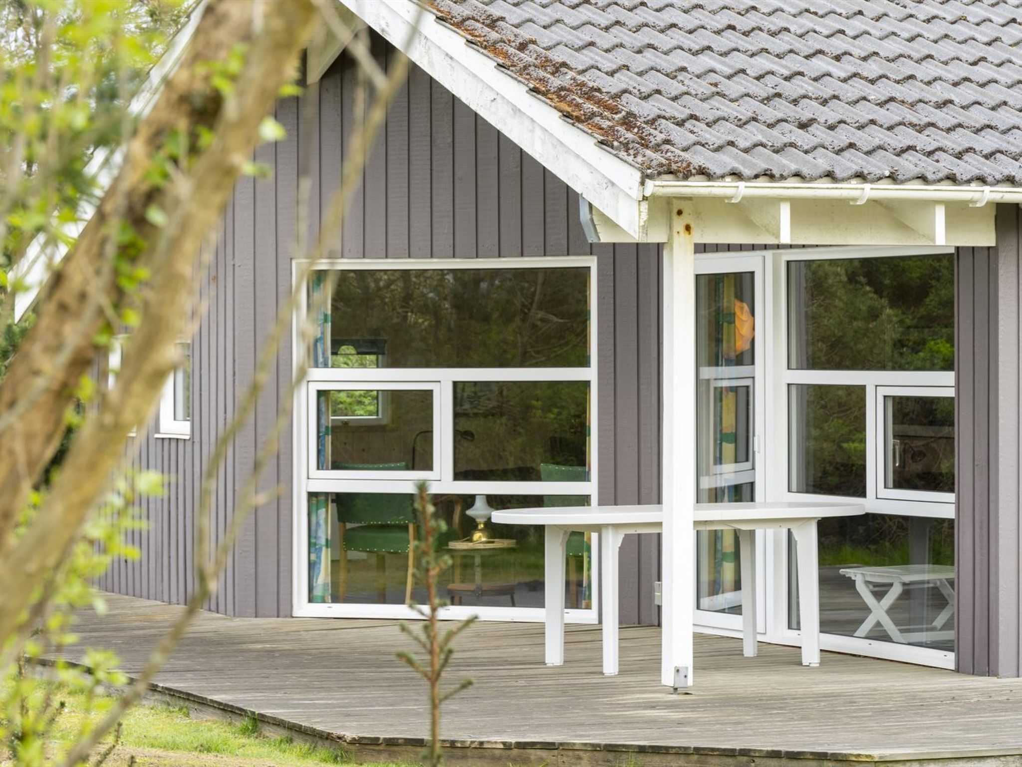 Una casa moderna con fachada gris, ventanas grandes y una terraza de madera.