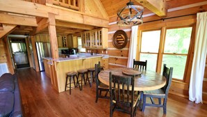 A wooden cabin interior with a dining area, kitchen, and a large window.