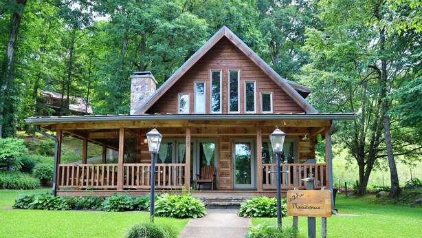 A wooden cabin with a porch, surrounded by lush greenery.