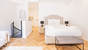 Une chambre moderne avec un grand lit, des lampes de chevet, un petit bureau et un escalier.