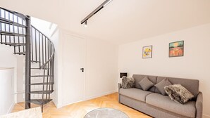 Un salon moderne avec un escalier à volutes, un canapé gris et deux œuvres d’art encadrées accrochées au mur.