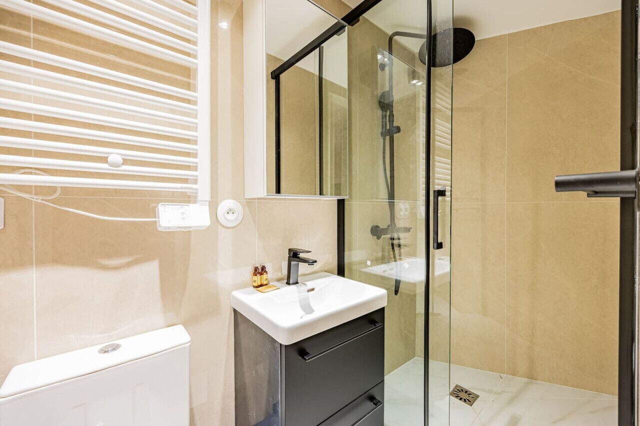 Et moderne badeværelse med en glasbrusekabine, en hvid vask og et lille toiletbord.