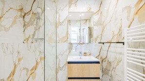 Une salle de bain moderne avec des murs en marbre, une douche en verre, un meuble-lavabo en bois et un porte-serviettes blanc.