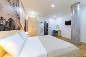 A modern hotel room with a large bed, a desk, a mirror, and a stone pillar.