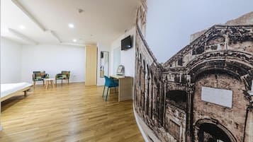 A room with a wooden floor, a bed, a desk with a chair, and a large wall mural of an ancient building.