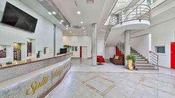 Un vestíbulo amplio con mostrador de recepción, una escalera y una gran pantalla de televisión.