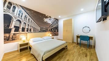 Un dormitorio con cama, escritorio, silla, televisor y un mural en la pared.