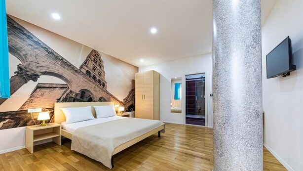 Une chambre avec un grand lit, un plancher en bois, un pilier en pierre, une télévision et une fresque représentant une arche.