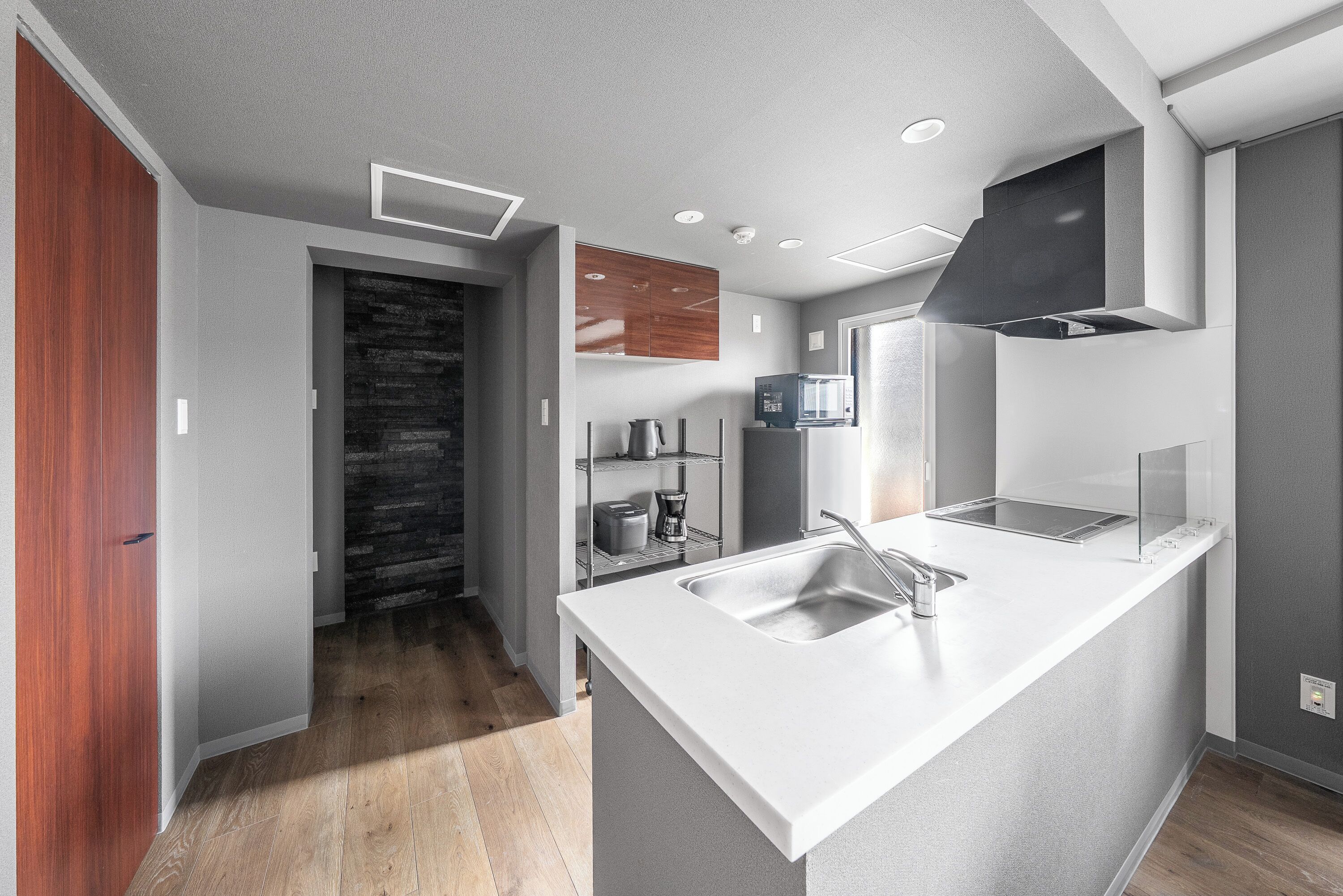A modern kitchen with a white countertop, stainless steel sink, and a black range hood.