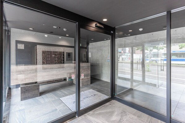 Un espace d’accueil moderne doté de portes vitrées, d’un comptoir de réception et d’un ascenseur bien visible.