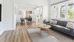 Un salon spacieux avec un canapé gris, un parquet et une grande fenêtre.