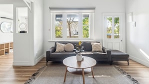 Un salon moderne avec un canapé gris foncé, une table basse ronde en bois et une grande fenêtre donnant sur la forêt.