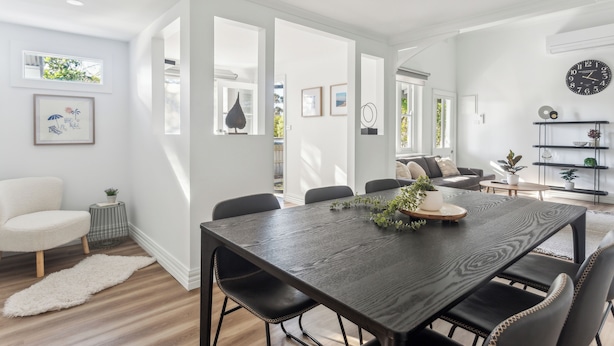 Un espace repas moderne avec une table en bois foncé, des chaises noires et un tapis blanc. Les murs sont ornés de tableaux encadrés et une horloge y est accrochée.