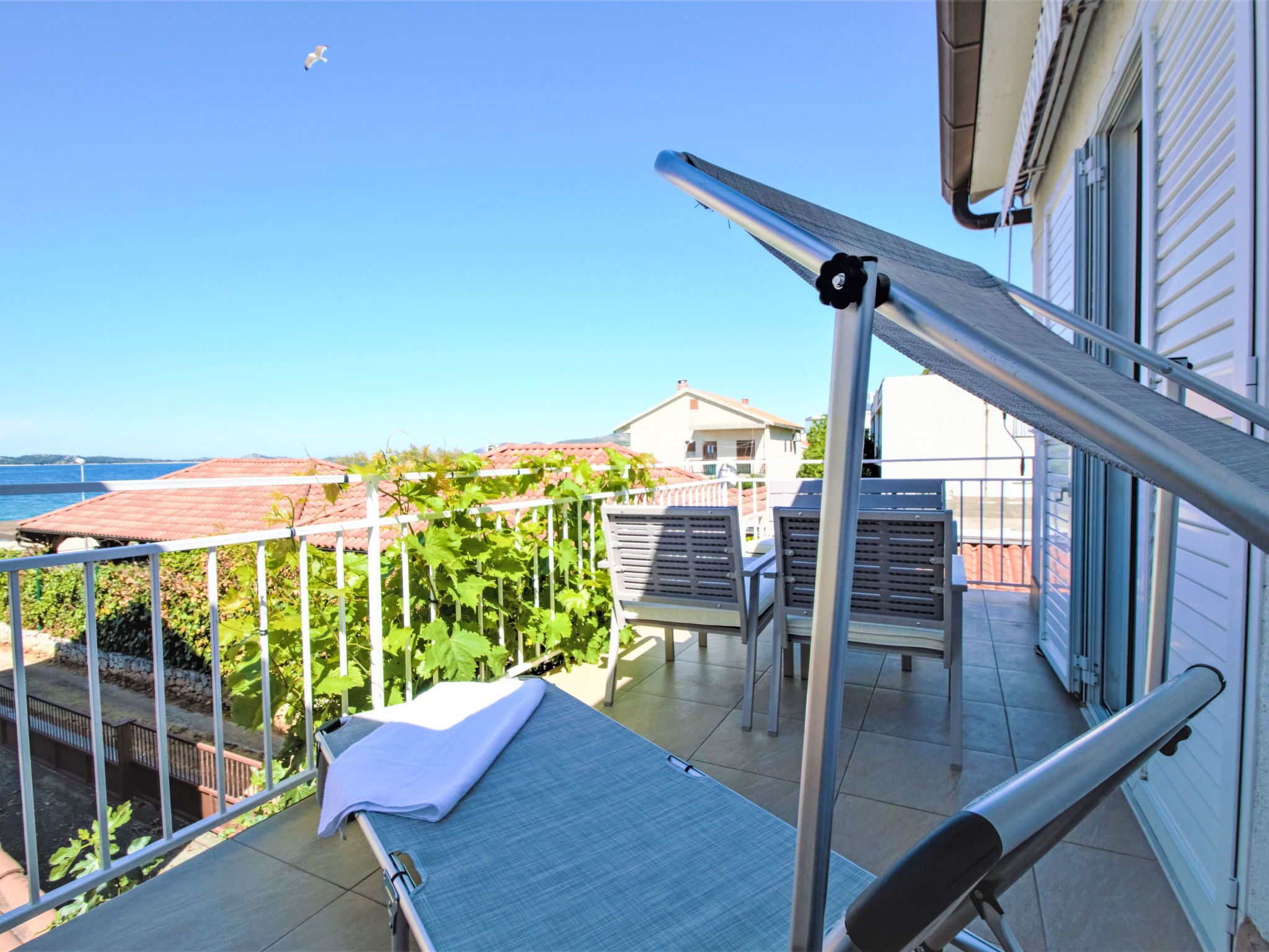 A balcony with a view of the sea, a pergola, and a table with a chair.