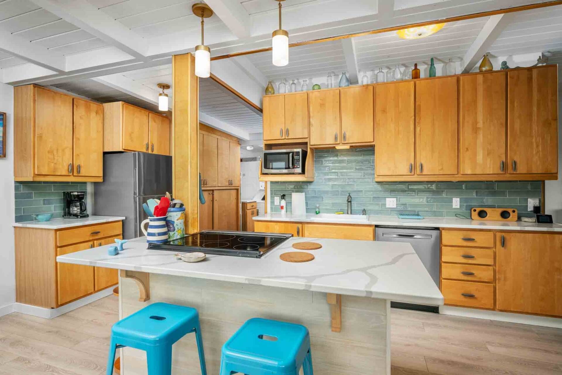 Une cuisine moderne avec des meubles en bois, un îlot central, des tabourets bleus et des luminaires suspendus.