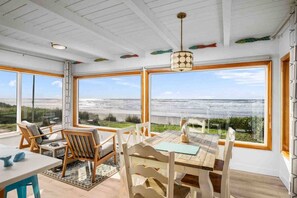 A room with large windows overlooking the ocean, wooden furniture, and a hanging light fixture. - Magnificent Oceanfront Retreat, Pet Friendly, Single Level, Deck and Fire-Pit w/ Views, EV Charging (Rockaway Beach)