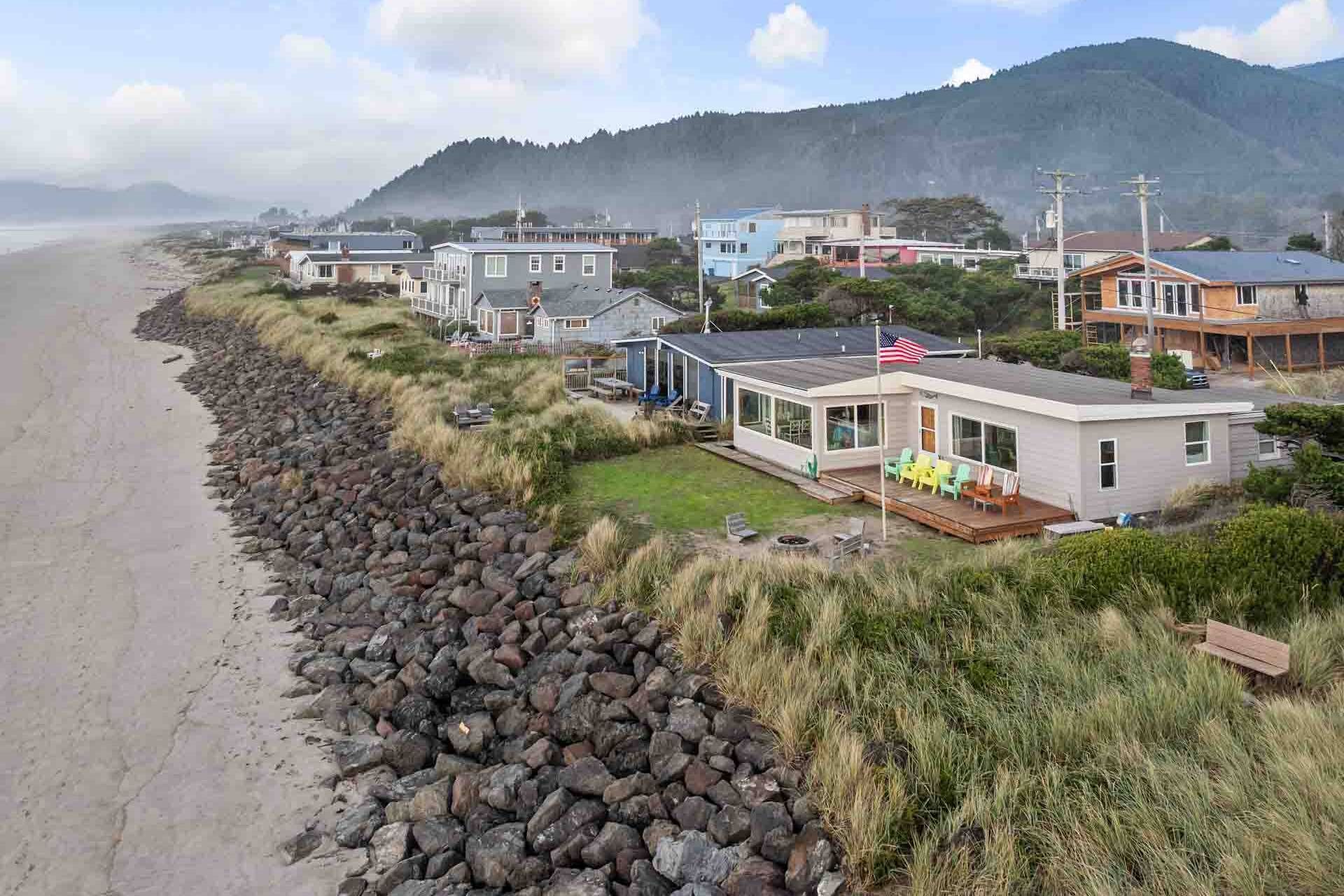 A coastal property with a stone wall, beach view, and houses with large windows and outdoor seating.