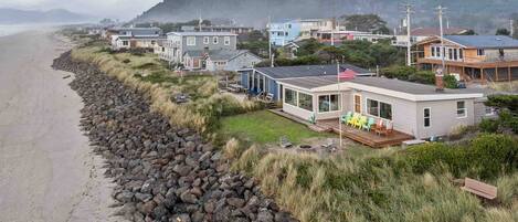 A coastal property with a stone wall, beach view, and houses with large windows and outdoor seating.