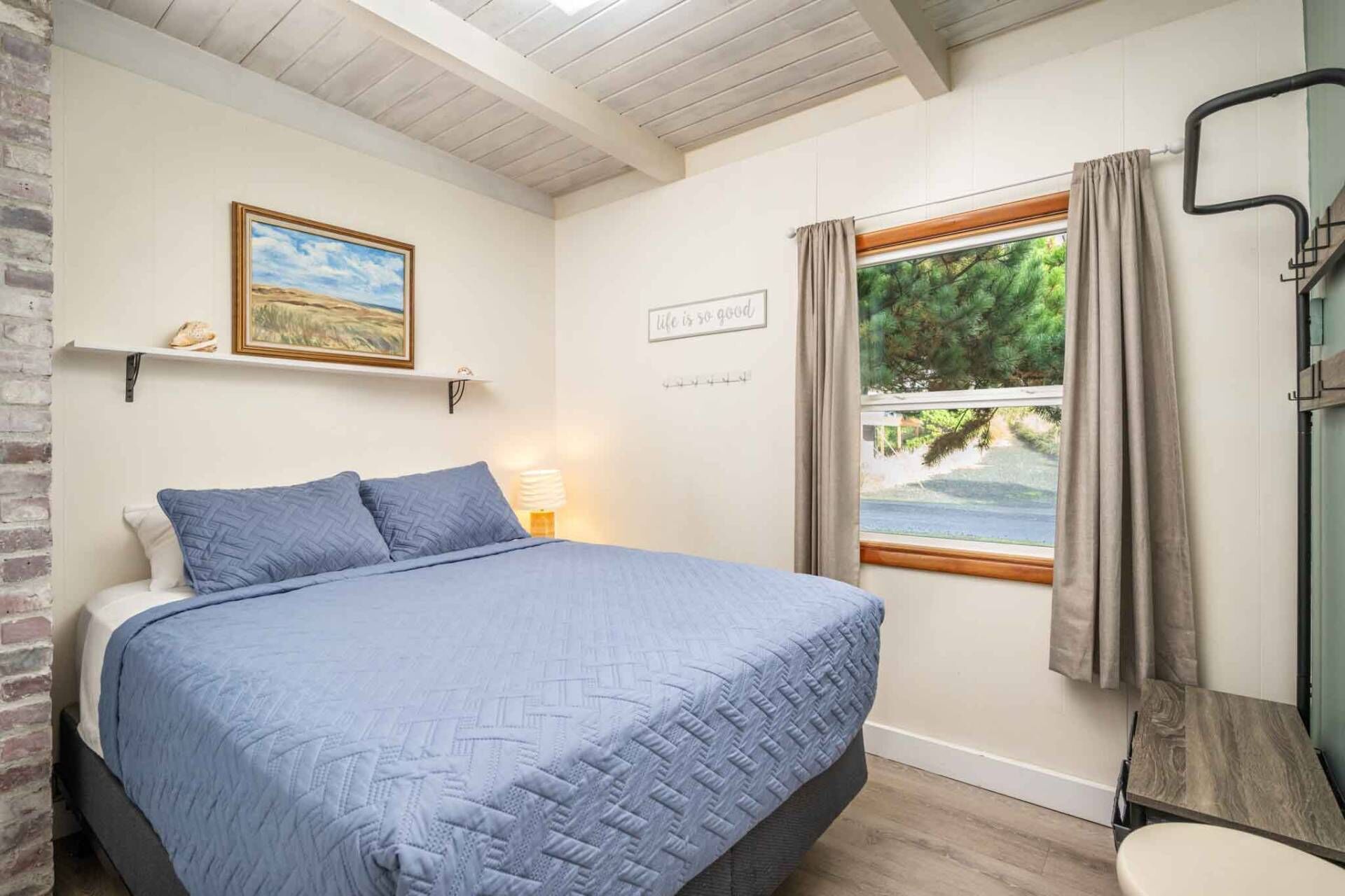 Une chambre à coucher avec un lit, une fenêtre avec des rideaux, un tableau au mur et une enseigne avec du texte.