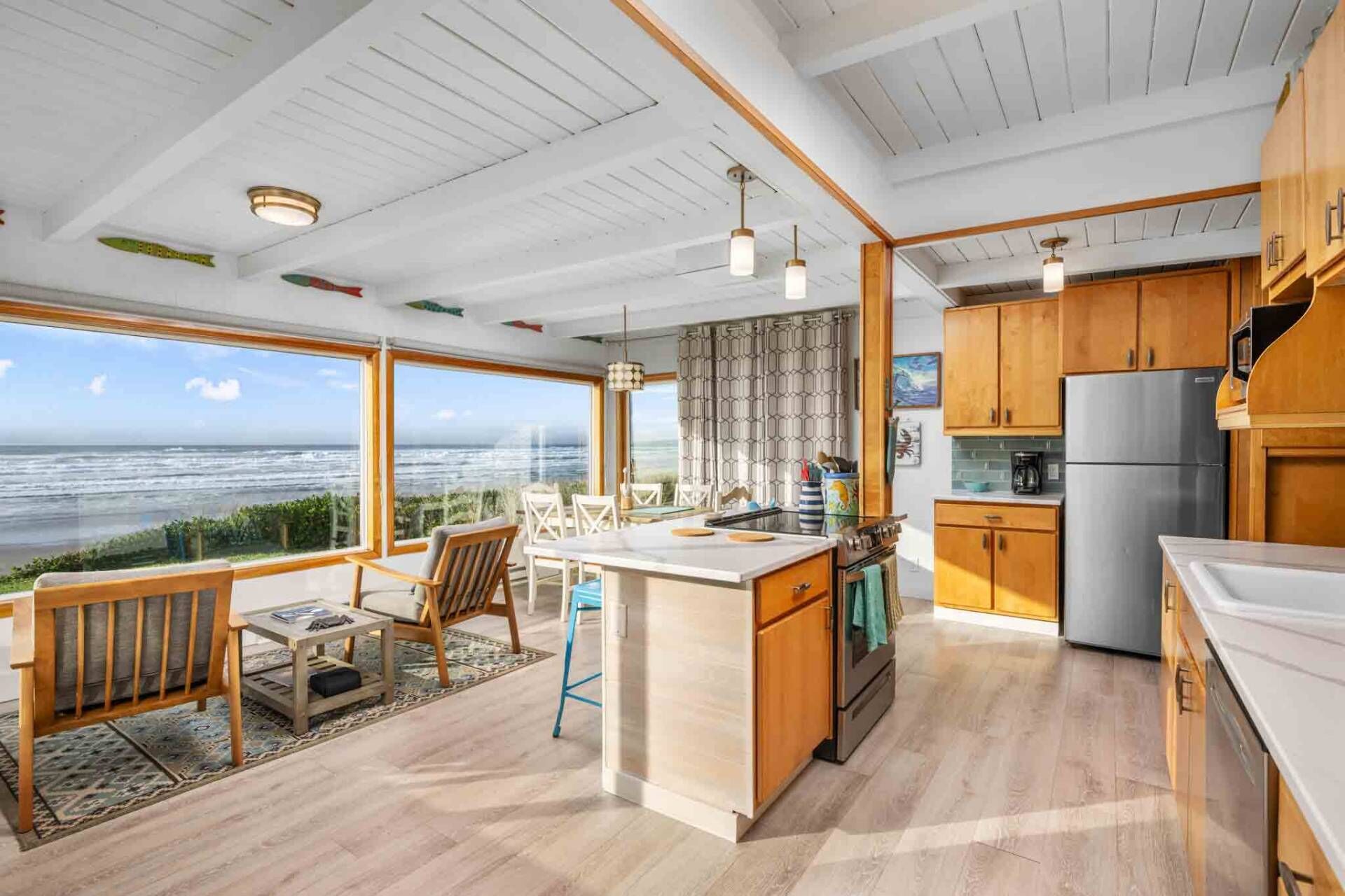 Una cucina moderna con mobili in legno, un frigorifero in acciaio inossidabile e un'isola grande. Si gode di una vista sull'oceano attraverso ampie finestre.