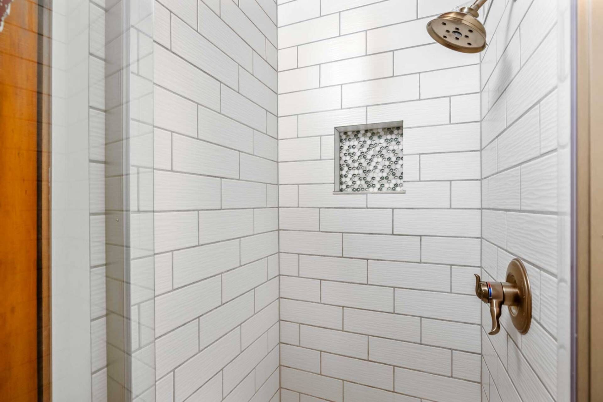 Ducha con azulejos blancos y un pequeño ventanal decorativo.