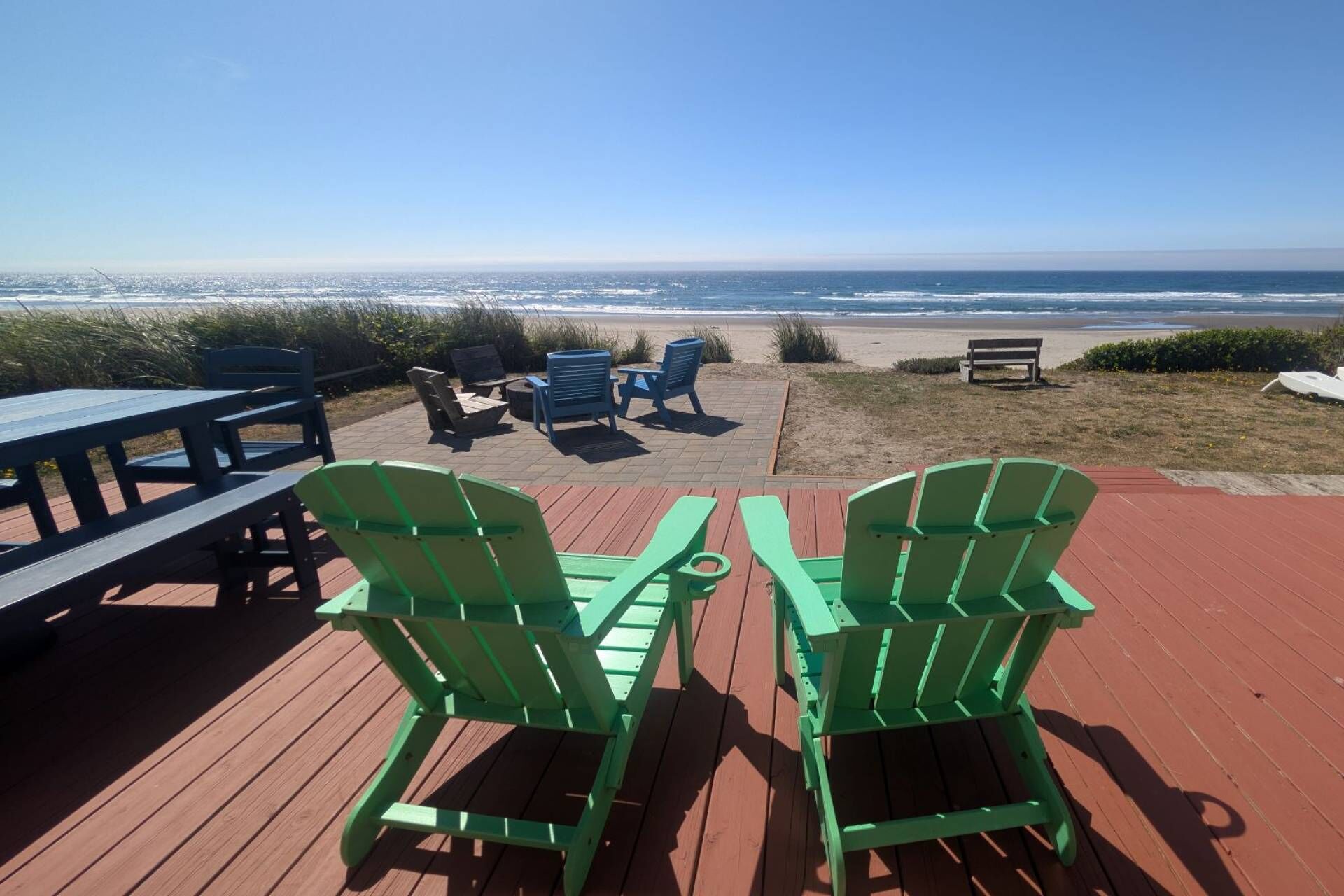 Een terras met groene Adirondack-stoelen, een picknicktafel en uitzicht op de oceaan.