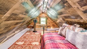 Una camera da letto mansardata con pareti in legno, un letto con copripiumino decorato, un tavolino e una ventola.