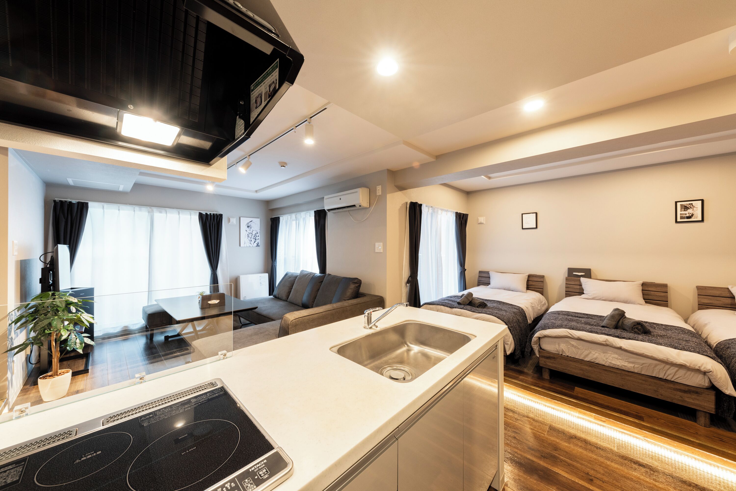 A compact hotel room with a kitchenette, a dining area, and two single beds.