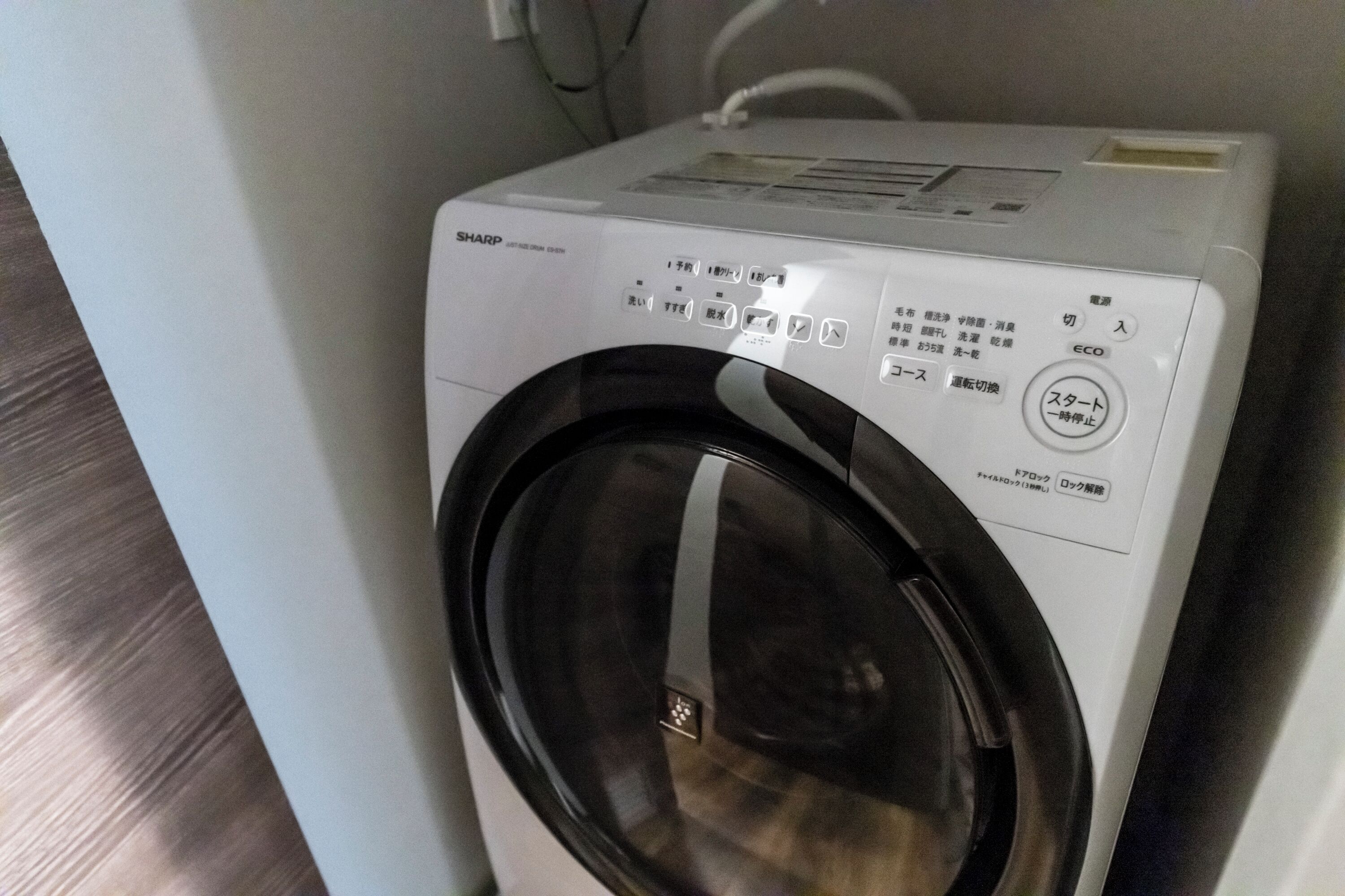 Vue de face d’un lave-linge Sharp blanc, doté d’un panneau de commande et d’une porte noire.