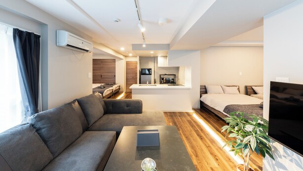 A modern hotel room with a sofa, a coffee table, a TV, a small kitchen area, and a bed. - NOBLE 302 (Sapporo)