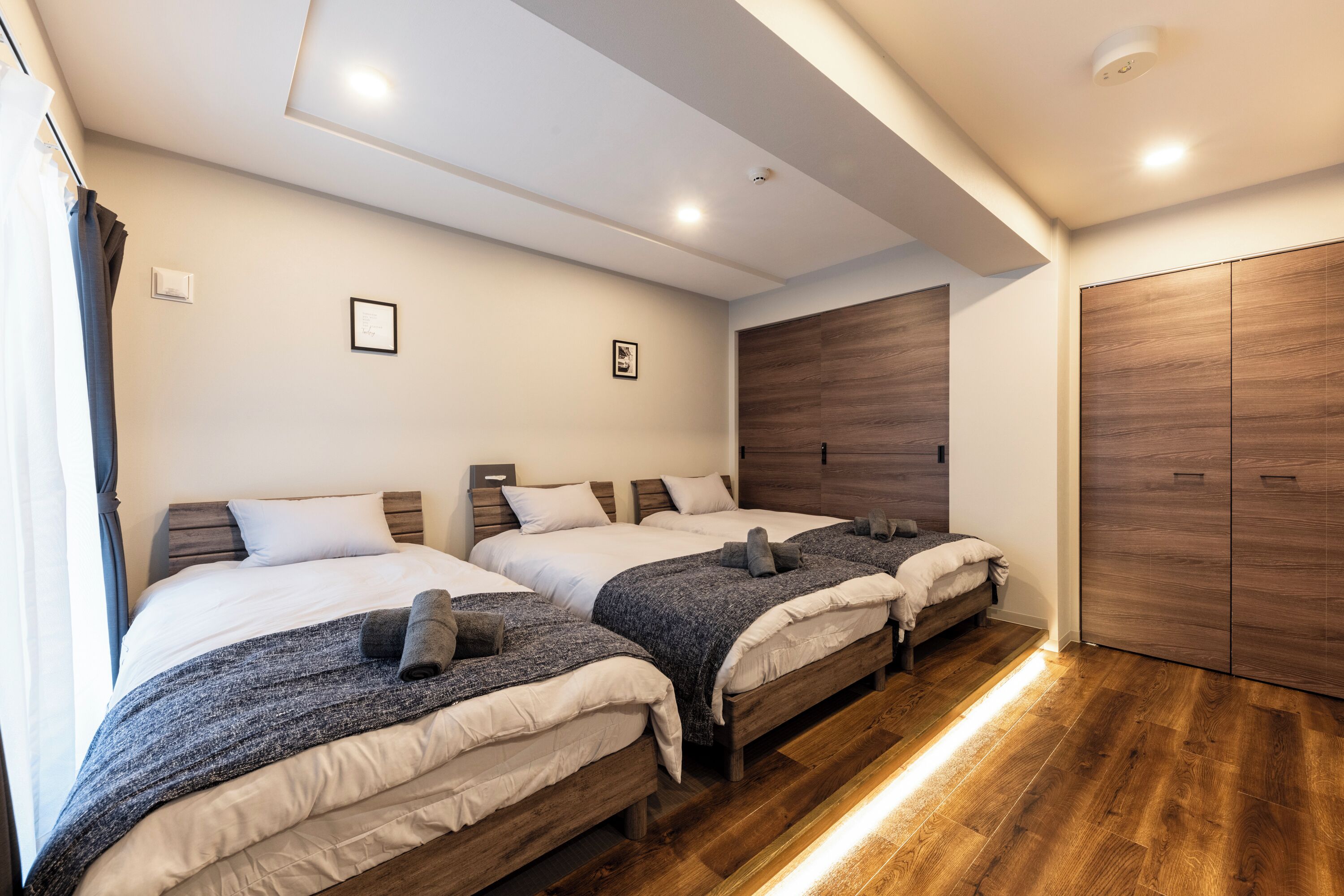 A hotel room with three beds, wooden flooring, and a wardrobe.