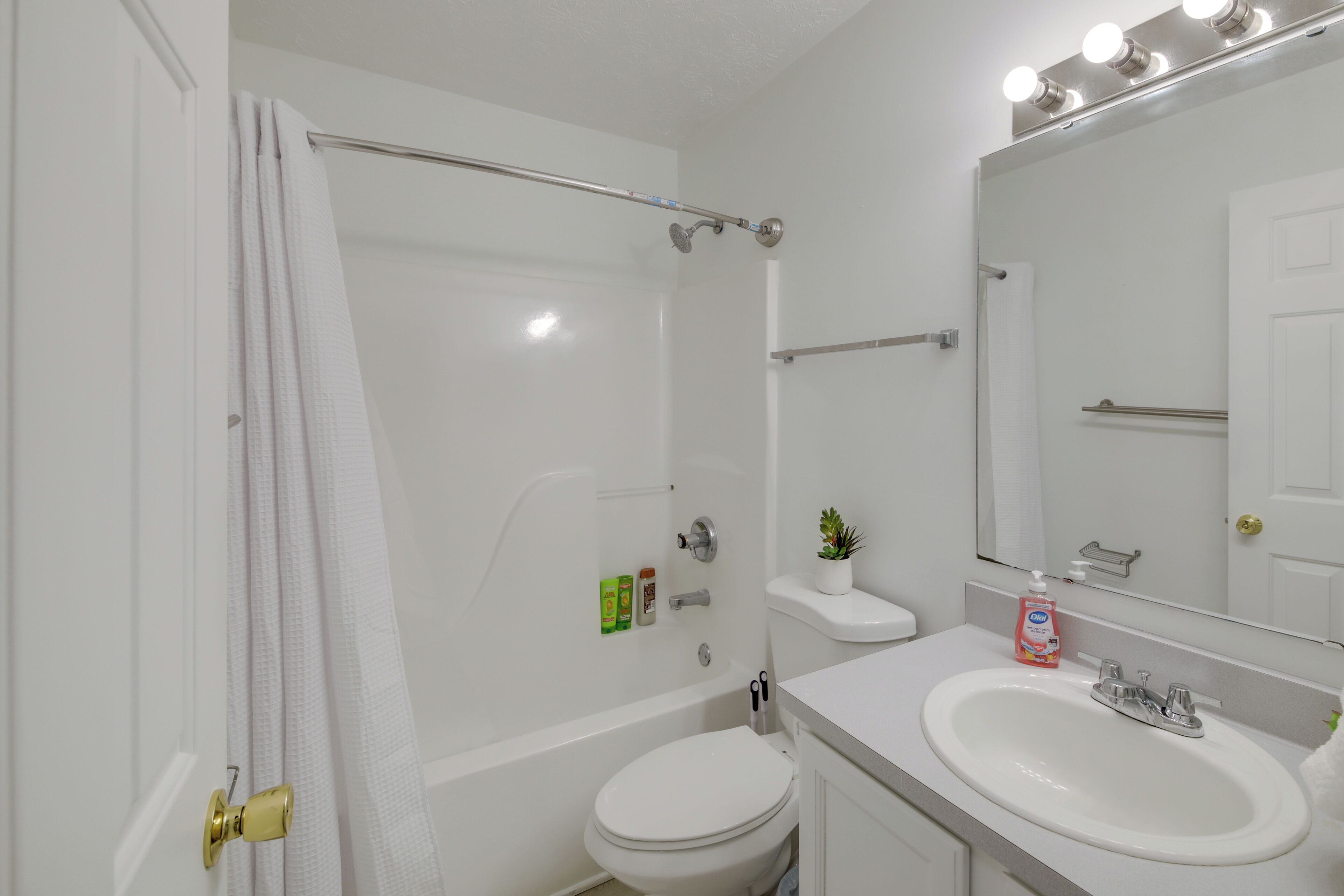 A bathroom with a bathtub, toilet, sink, and a mirror with lights.