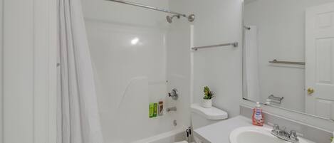 A bathroom with a bathtub, toilet, sink, and a mirror with lights.