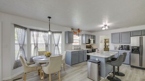 A modern kitchen with grey cabinets, a stainless steel refrigerator, and a central island with bar stools. - Family-Friendly Indianapolis Home w/ Fenced Yard (Indianapolis)