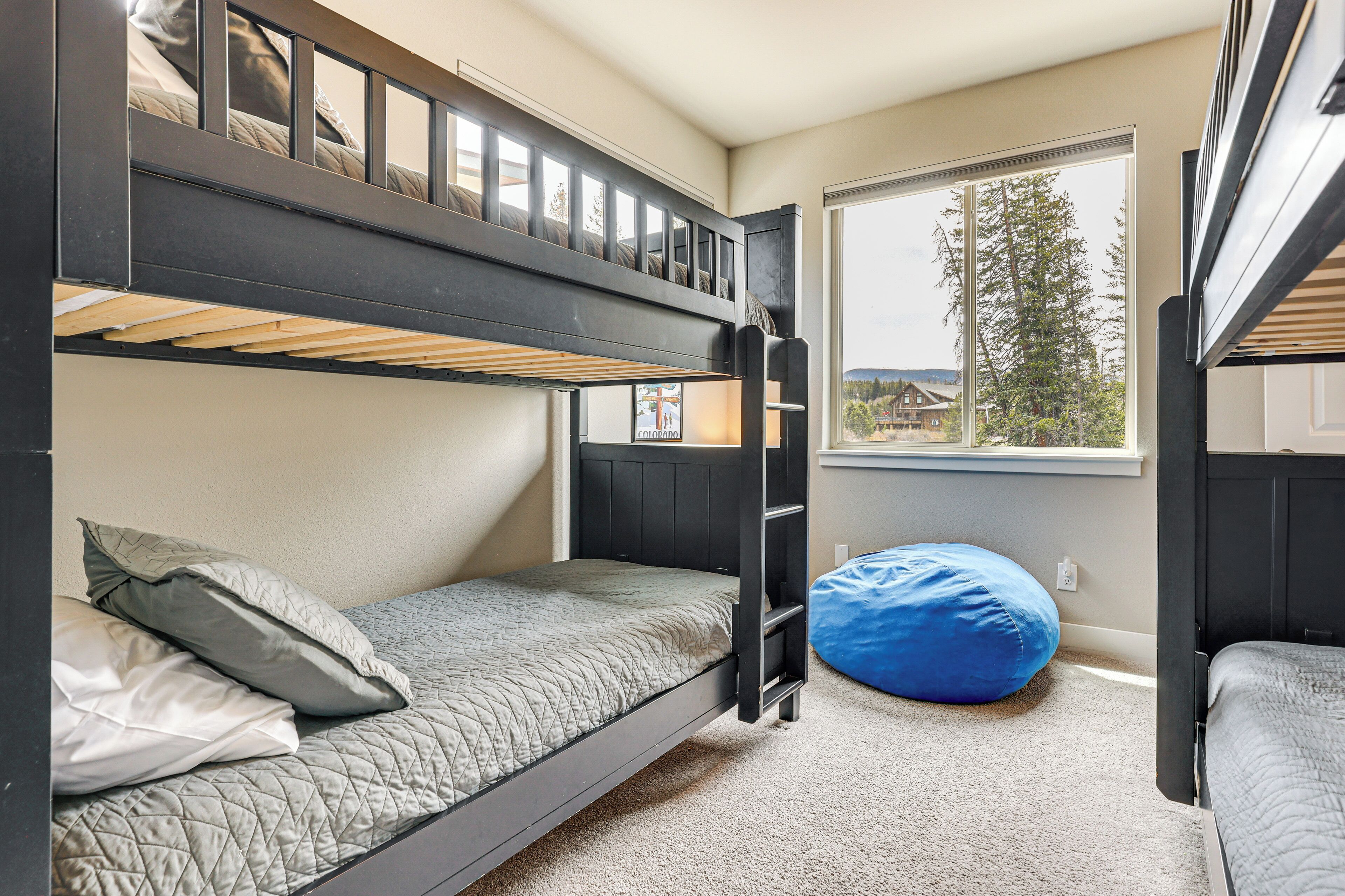 Une chambre avec un lit superposé, une fenêtre donnant sur l’extérieur, un pouf bleu et une porte.