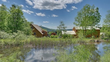 Escape to a serene lakeside retreat with two traditional cabins surrounded by lush greenery and a peaceful body of water.