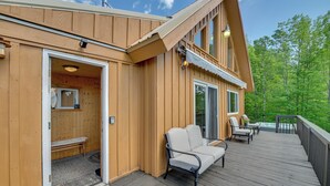 En træhytte med en terrasse, et overdækket udendørs opholdsområde og en dør, der fører til et indre rum.