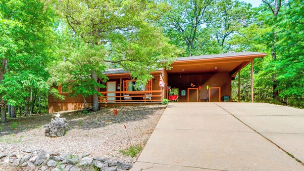A lodge with a covered porch, a stone pathway, and a forested backdrop. - Hot Tub & Fire Pit: Holiday Island Getaway! (Holiday Island)