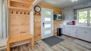 A wooden interior with a bench, a door, a clock, a microwave, and cabinets. - Lakefront Home in Hartford: Hot Tub, Kayaks & Dock (Hartford)