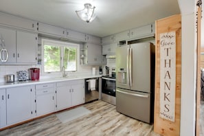 Una cocina moderna con armarios blancos, electrodomésticos de acero inoxidable y un letrero de madera que dice "Give Thanks".
