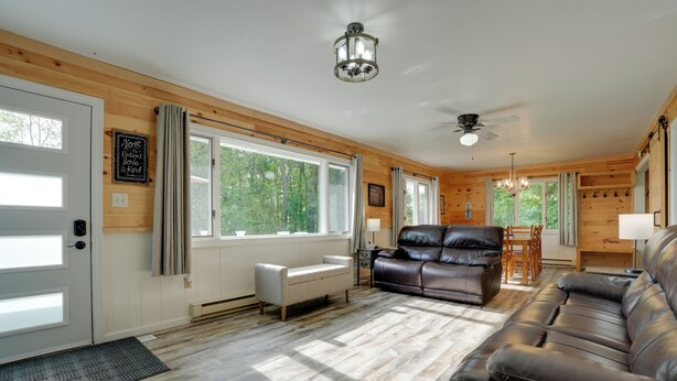 A spacious living room with a fireplace, leather sofas, and large windows offering a view of the outdoors. - Lakefront Home in Hartford: Hot Tub, Kayaks & Dock (Hartford)