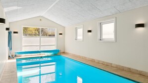 Ein Hallenbad mit klarem, blauem Wasser, gefliestem Boden und einer hohen Decke mit geometrischem Muster.