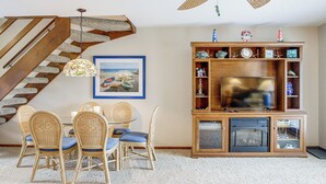 A living room with a wooden staircase, a dining table with chairs, a television, and a fireplace.