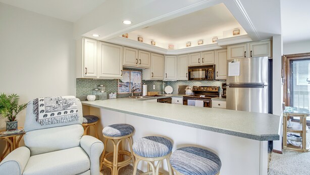 A spacious kitchen with white cabinetry, a large island with bar stools, and stainless steel appliances.